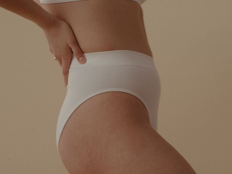 devojka pozira u belim gaćicama, neutralna krem pozadina