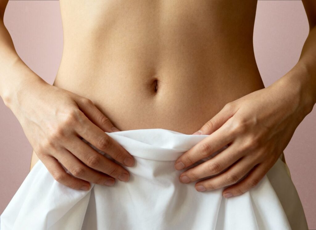 devojka drži neznu svilu preko svog golog tela bele boje, pozadina rozikasta