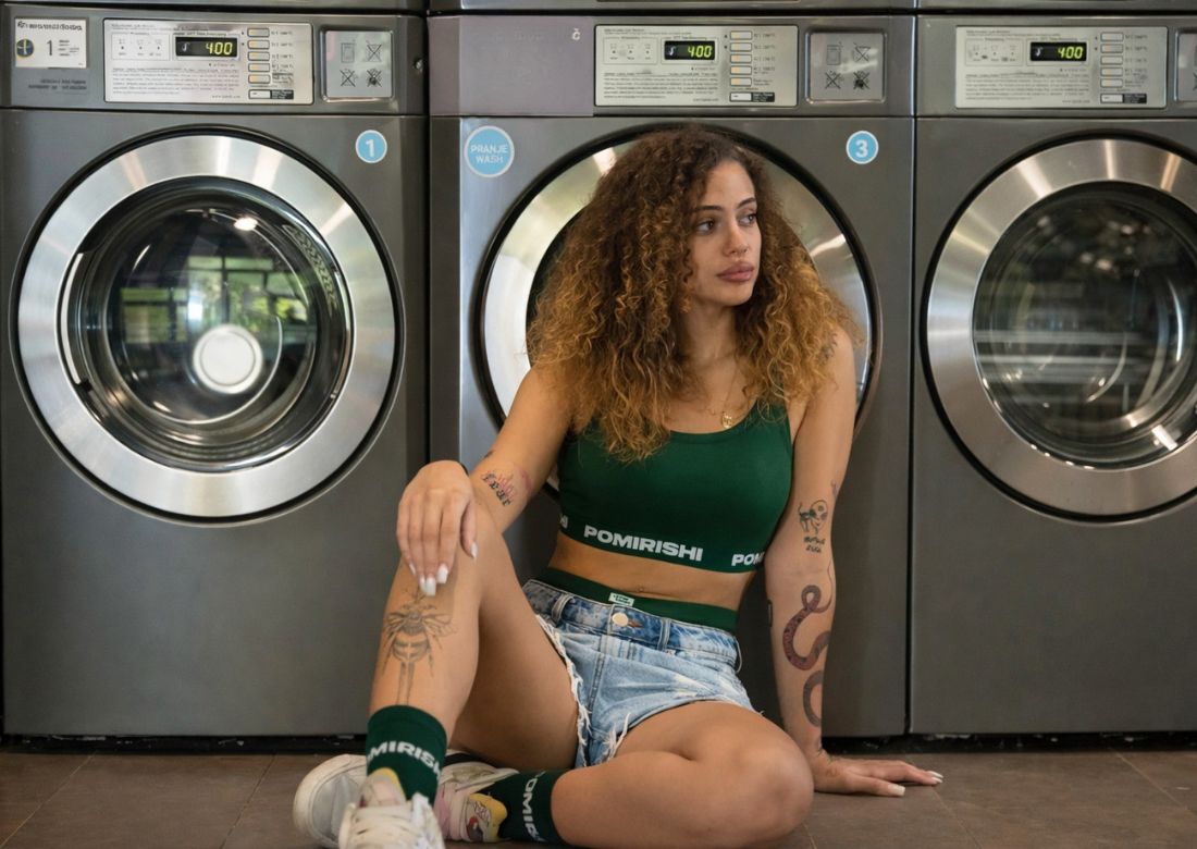 devojka sedi na podu u pomirishi setu vešu od bambusa zelene boje naslonjena na mašinu za sušenje veša