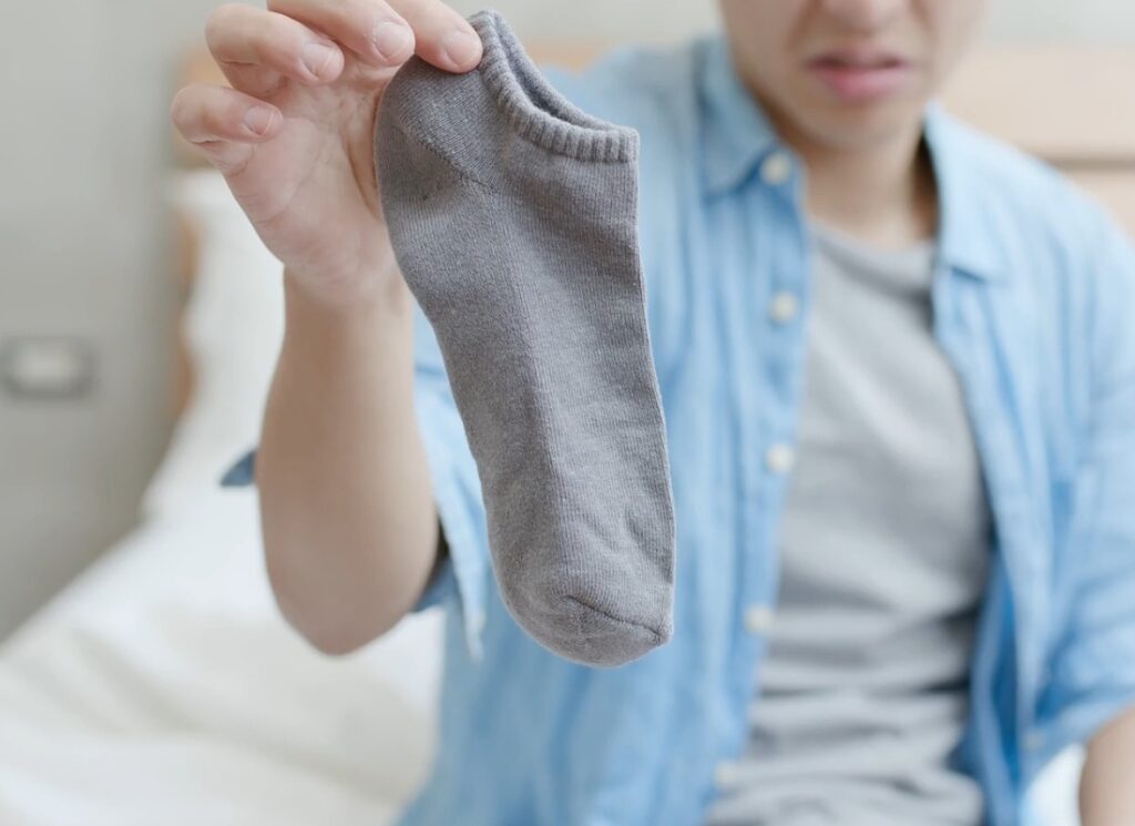 prikaz muškarca u svetlopavoj košulji i beloj majici koji drži sivu nazivicu čarapu u ruci